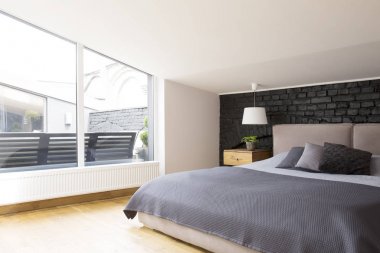 Yatakta siyah tuğla duvara gri yatak takımları ile ferah yatak odası iç içinde pencere eşiği