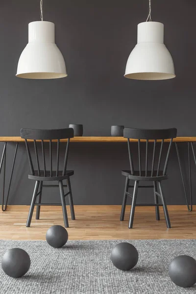 两盏白色的灯挂在黑色室内的木餐桌上 地板上有球饰 — 图库照片