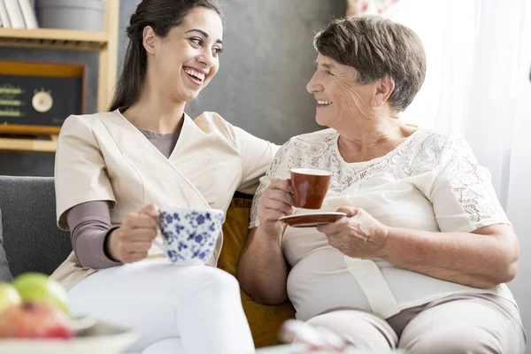 微笑的志愿者喝咖啡与资深病人在养老院 — 图库照片