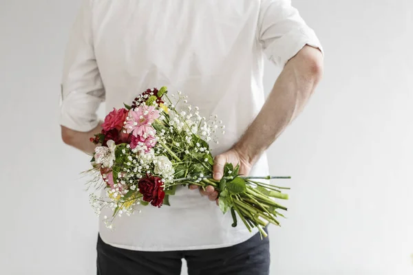 彼の日の彼の背中の後ろに春の花のブーケを持ってエレガントな男 — ストック写真