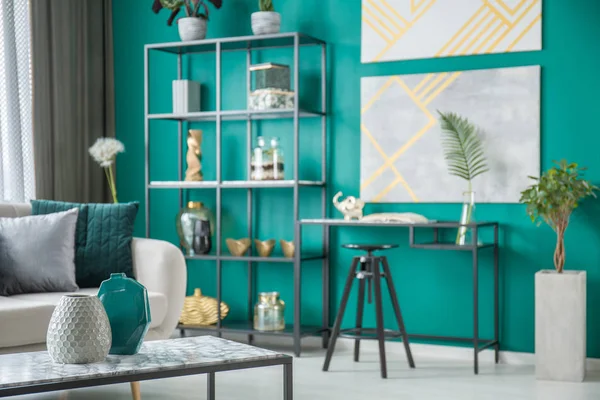 Black chair at desk against green wall with gold posters in living room interior with vases