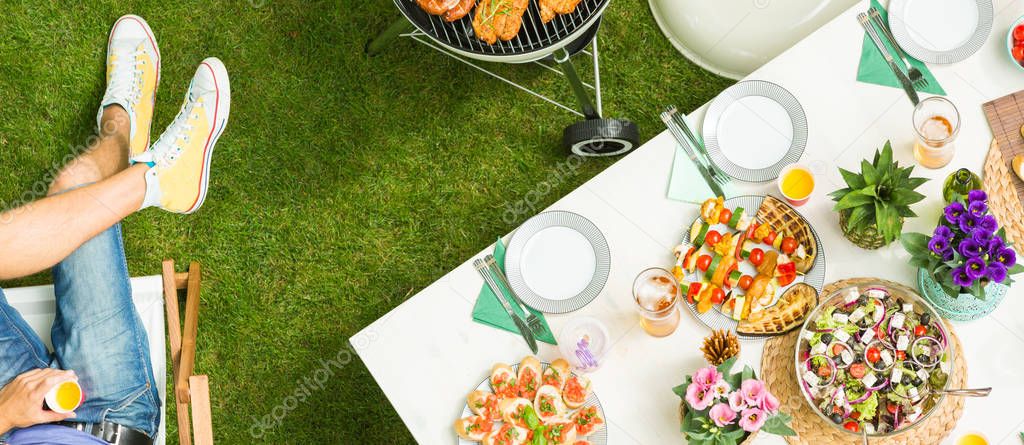 Food on the table and man holding a drink - grill party from the top