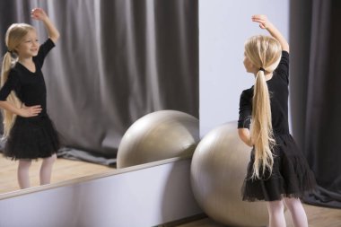 Blonde girl dancing in front of the mirror during a ballet lesson for youth clipart