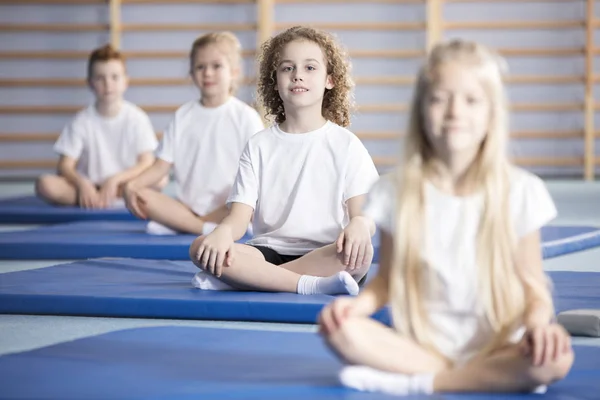 在一个矫正体操课上坐在蓝色垫子上的微笑的男孩和朋友 — 图库照片