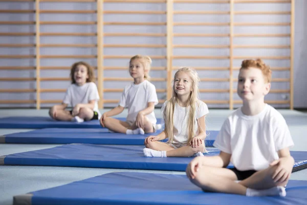 Focused pupils sitting cross-legged on blue mats during gymnastics class