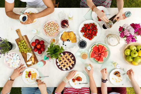 Friends having outdoor meal eating fruit, pie, cheese and drinking coffee in the garden