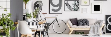 Beyaz bisiklet, yemek masası ve taze bitkiler ile oturma odası iç duvarında asılı basit posterler