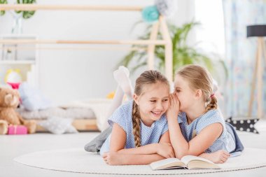 Konuşuyor, gülüyor ve birbirlerine beyaz bir halı üzerinde uzanmış bir odada sırlarını anlatmaya iki kız