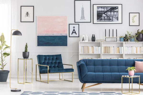 Navy blue sofa against bookshelf and white wall with pink painting in elegant living room interior