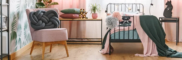 两个灰色和粉红色的彩球挂在一个金属床框架在舒适的卧室内与结垫在扶手椅上 — 图库照片