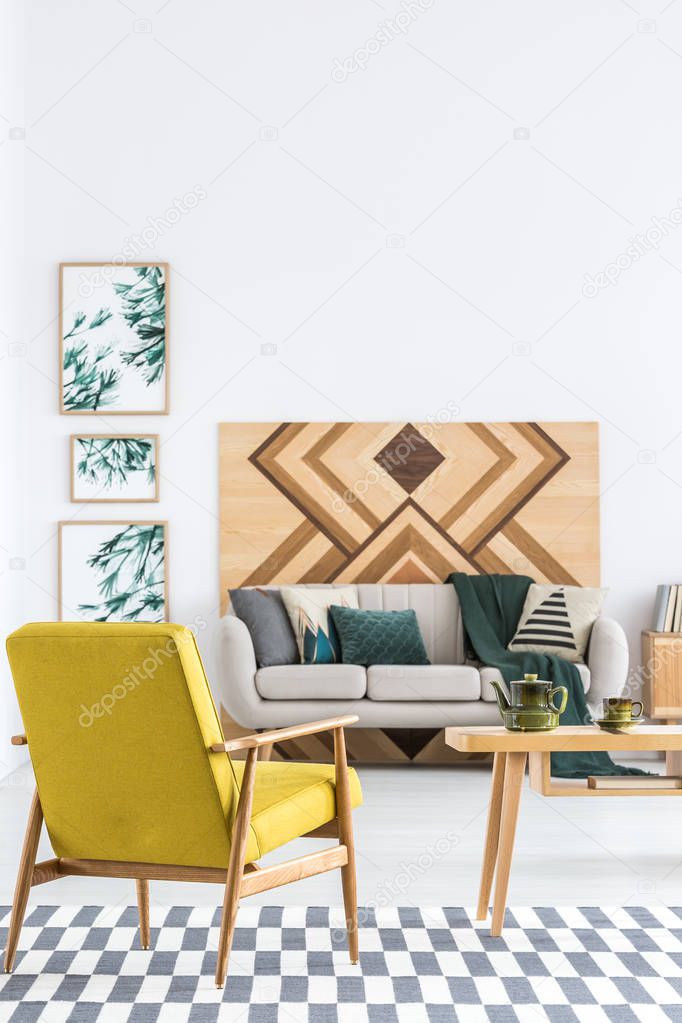 Yellow armchair on patterned carpet in spacious living room interior with woodworking on the wall