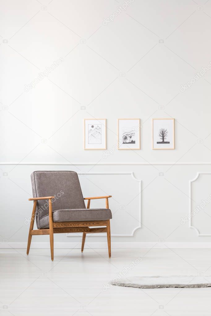 Grey armchair against white molding wall with posters in simple living room interior