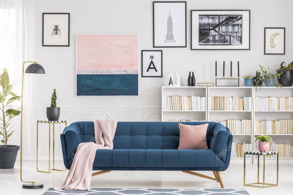 Pink blanket on navy blue sofa in modern living room interior with gallery of posters on the wall