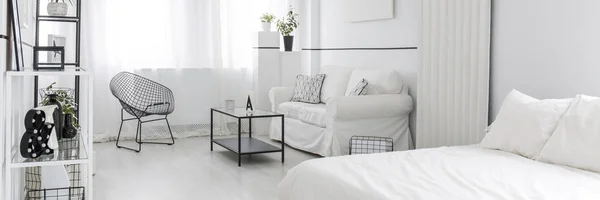 White, open space apartment interior for a single woman with black armchair standing next to the window near a sofa and black coffee table