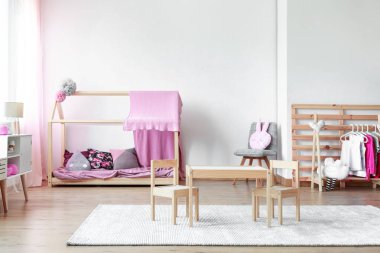 Süslü, pembe ve parlak bebek odasındaki boş beyaz duvara ahşap mobilyalar kopyala