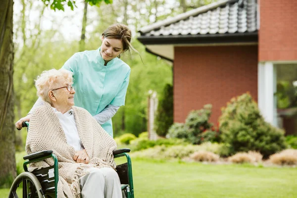 Mujer discapacitada mayor con cuidador en el jardín del hogar de ancianos — Foto de Stock