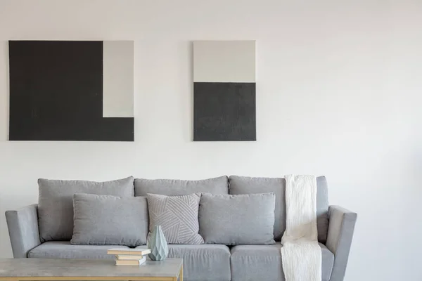 Pintura abstracta en blanco y negro en la pared vacía del elegante salón interior con cómodo sofá gris con almohadas — Foto de Stock