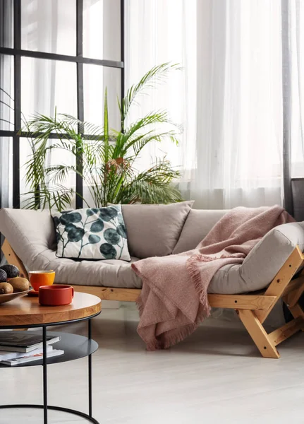 Petite table basse devant un canapé futon scandinave avec oreiller à motifs et couverture rose patel — Photo