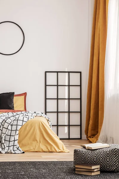 Griglia in legno nero accanto al letto con biancheria da letto arancione in camera da letto con pareti bianche — Foto Stock