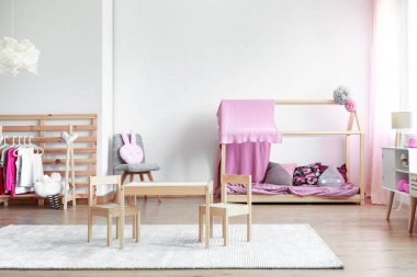 Moda pembesi ve parlak kız odasındaki boş beyaz duvara tahta mobilyalar ve oyuncaklar kopyala