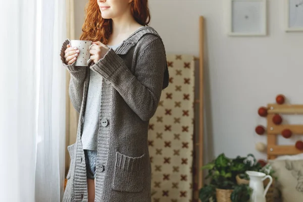 Hermosa chica pelirroja vistiendo suéter gris cálido y sosteniendo taza de café — Foto de Stock