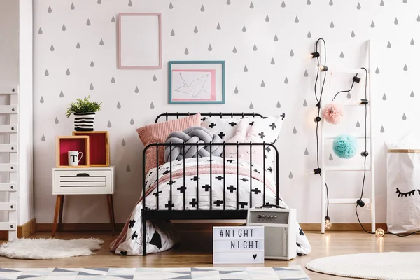 Pompones y luces azules y rosadas en la escalera escandinava blanca de madera en el elegante interior del dormitorio con ropa de cama en blanco y negro, mesita de noche pequeña y marcos en el suelo —  Fotos de Stock