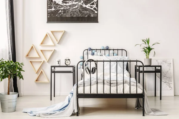Black map on white wall of fashionable kid 's bedroom with industrial single bed and nightstand with clock and cup — стоковое фото