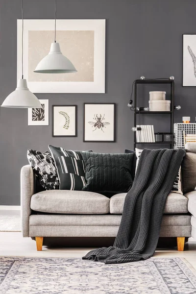 Manta oscura y almohadas en sofá esquinero gris en el interior de la sala de estar contemporánea con pared gris y muebles industriales —  Fotos de Stock