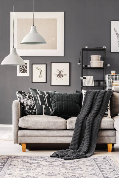 Dark blanket and pillows on grey corner sofa in contemporary living room interior with grey wall and industrial furniture — Stock Photo, Image