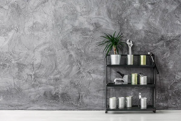 Schwarzes Industrieregal mit Dosen, Werkzeugen und Pflanzen auf grauer Betonwand, echtes Foto mit Kopierraum — Stockfoto