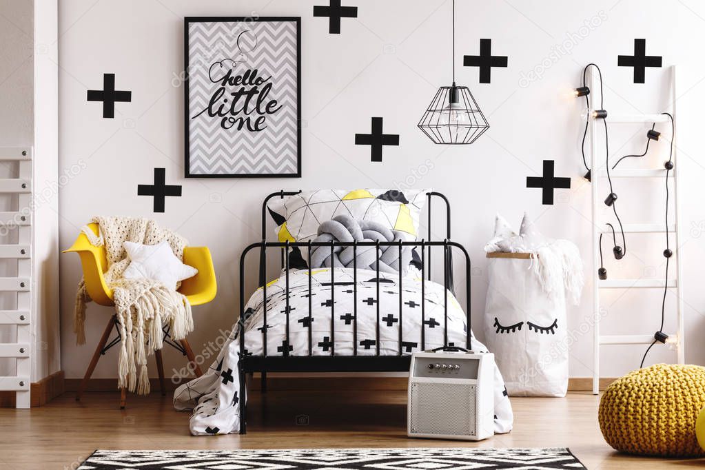Star shape pillow and white woolen blanket on yellow chair next to industrial single black metal bed with bedding and knot pillow in fashionable bedroom for kid