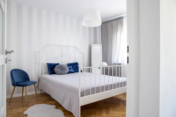 Chaise bleue tendance à côté du lit king size avec des oreillers dans l'intérieur élégant de la chambre — Photo