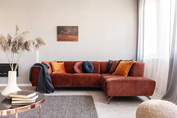 Foto real de almofadas de cor quente em um sofá vermelho ao lado da janela no interior acolhedor da sala de estar — Fotografia de Stock