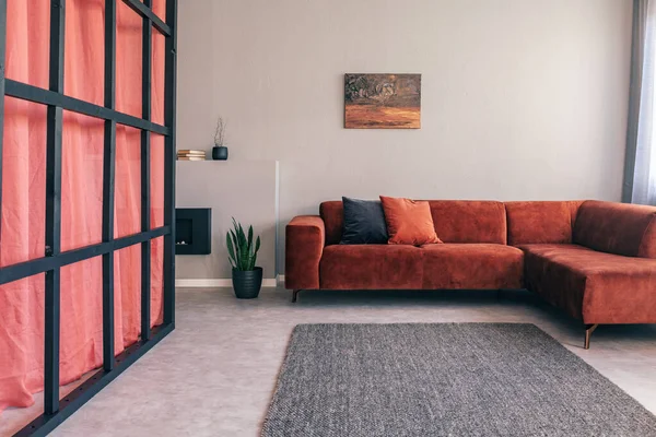 Skutečná fotografie jednoduchého interiéru obývacího pokoje s červenou rohovou pohovkou, černou obrazovkou a šedým kobercem — Stock fotografie
