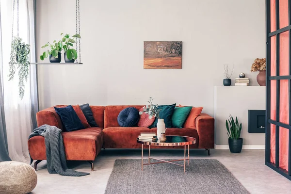 Real photo of colorful pillows on a red corner couch in white living room interior with gray rug — Stock Photo, Image