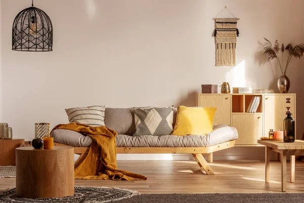 Безделушки на деревянном комоде за серым диваном с подушками и одеялом — стоковое фото