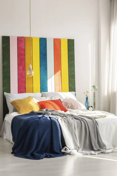 Лампочка над уютной кроватью с подушками и одеялами в светлом интерьере спальни — стоковое фото