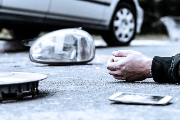 Mão humana no chão ao lado do espelho do carro quebrado e telefone celular após um acidente — Fotografia de Stock