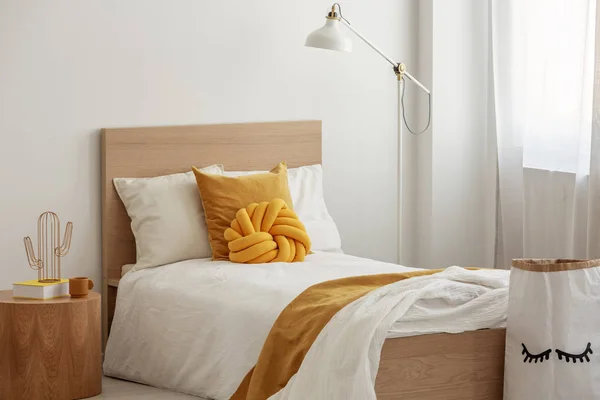 Alta lampada industriale sopra cuscini gialli e coperta su letto singolo in legno bianco — Foto Stock