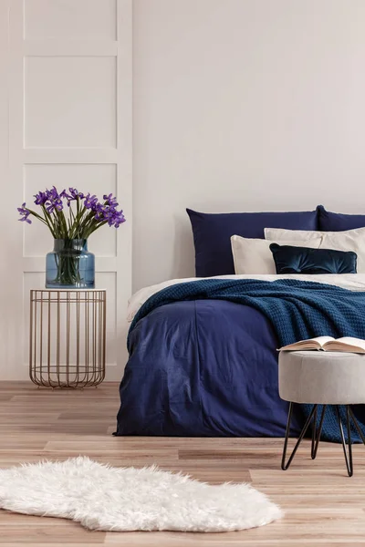 Fleurs violettes dans un vase en verre bleu sur une table de chevet élégante à côté du lit king size — Photo