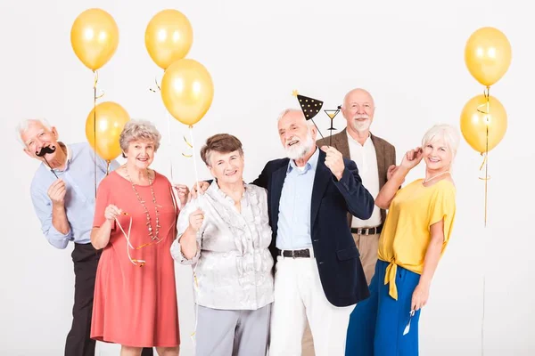 Group of happy senior friends holding yellow balloons and standing in white interior — Stock Photo, Image