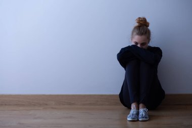 Katta, kopya alanı boş duvara oturan karanlık kıyafetlerle anksiyete bozukluğu olan genç kadın