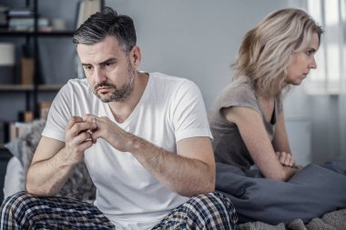 Pijamalı bir adam yatakta oturuyor ve karısıyla tartıştıktan sonra alyansını çıkarıyor.