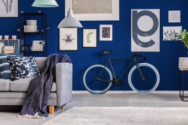 Duvarında ilham verici bir poster olan mavi oturma odası ve klasik zümrüt yeşili bisiklet.