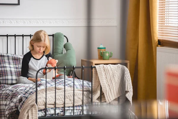 Linda niña sentada en su cama de metal individual en el interior del dormitorio de moda para el niño —  Fotos de Stock