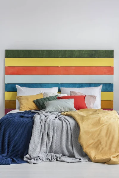 色彩艳丽的床，有枕头、毛毯和有彩虹色木材的床头 — 图库照片