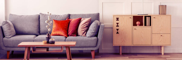 Wooden furniture and grey scandinavian sofa with pillows in beautiful living room interior