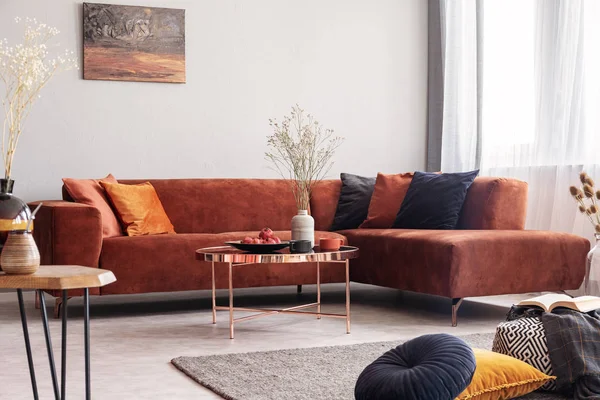 Foto real de uma mesa de ouro rosa no interior da sala de estar quente com muitas almofadas e um sofá de canto — Fotografia de Stock