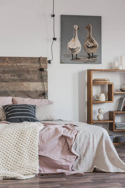Real photo of a bright, rustic bedroom interior with pink bed, wooden furniture and painting of two ducks — Stock Photo, Image