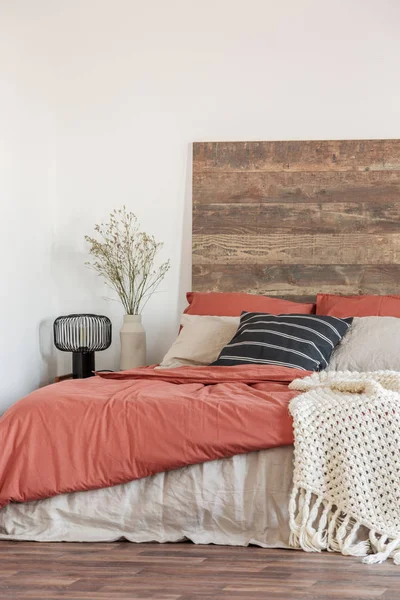 Acogedor dormitorio interior con paredes blancas, cabecera de madera y sábanas rojas. Foto real —  Fotos de Stock